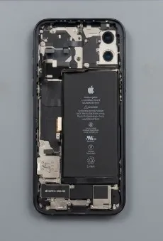 Un iPhone ouvert, coque arrière retirée, batterie et nappes visibles sur un plan de travail